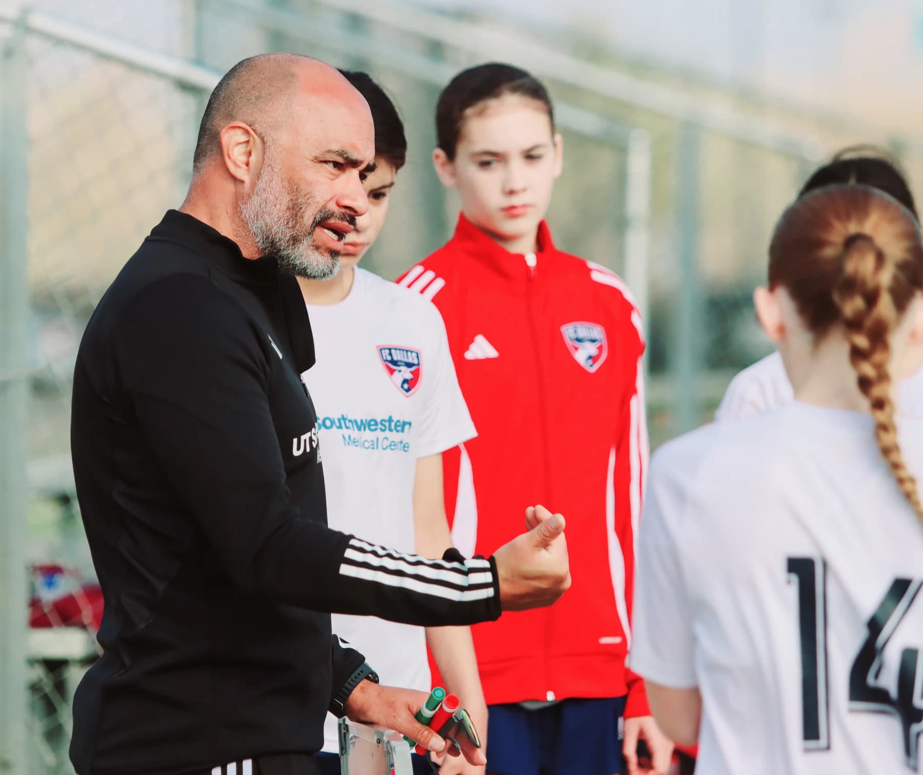Alberto Carbajal giving guidance to FC Dallas Youth girls players beside the pitch