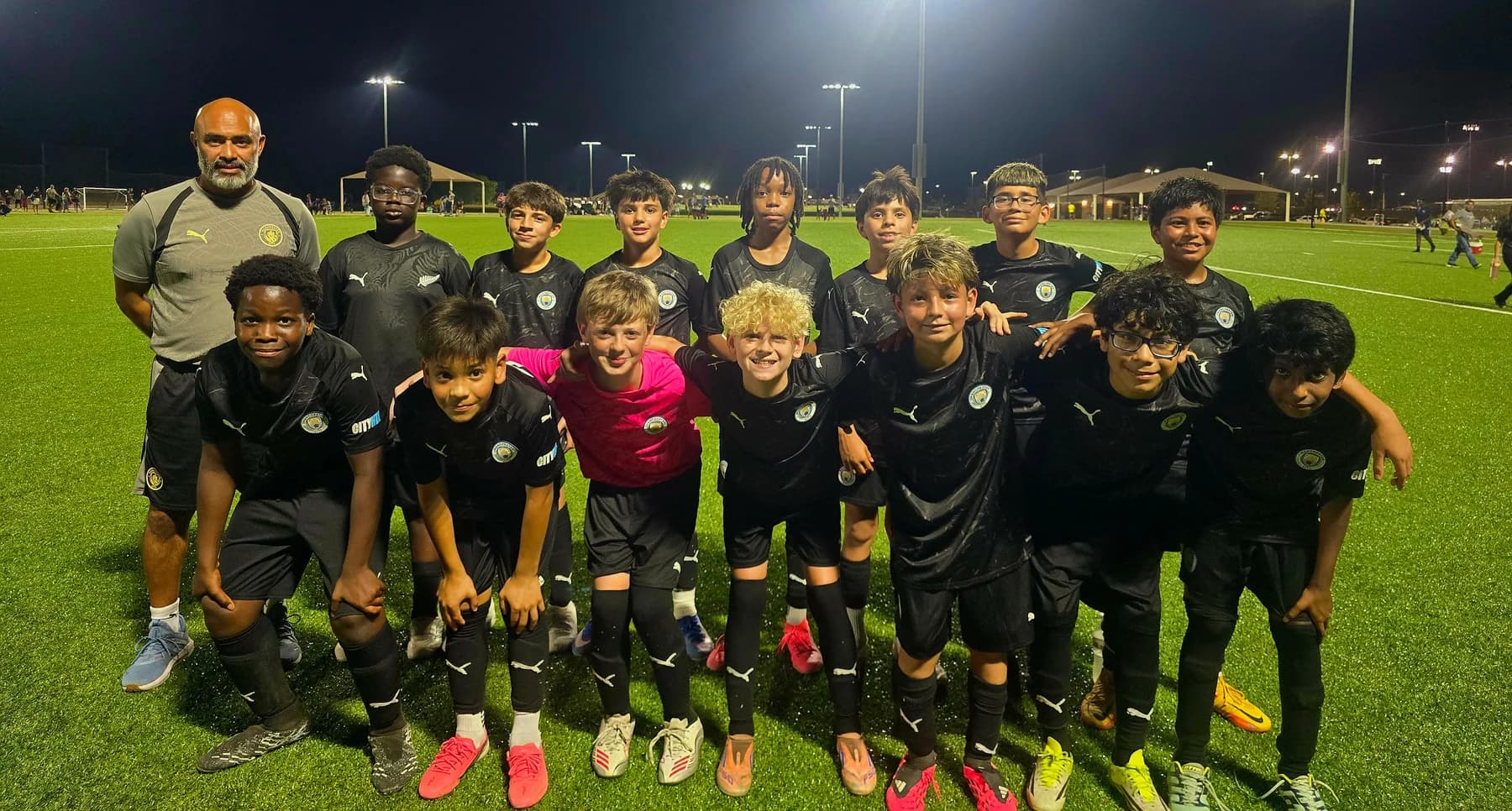Coach Alberto Carbajal with his Manchester City North Texas FC U13 team on a floodlit pitch